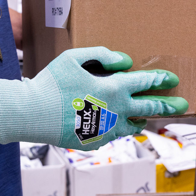 Gloved hand wearing the Helix 3050 abrasion-resistant gloves handling cardboard packaging box.