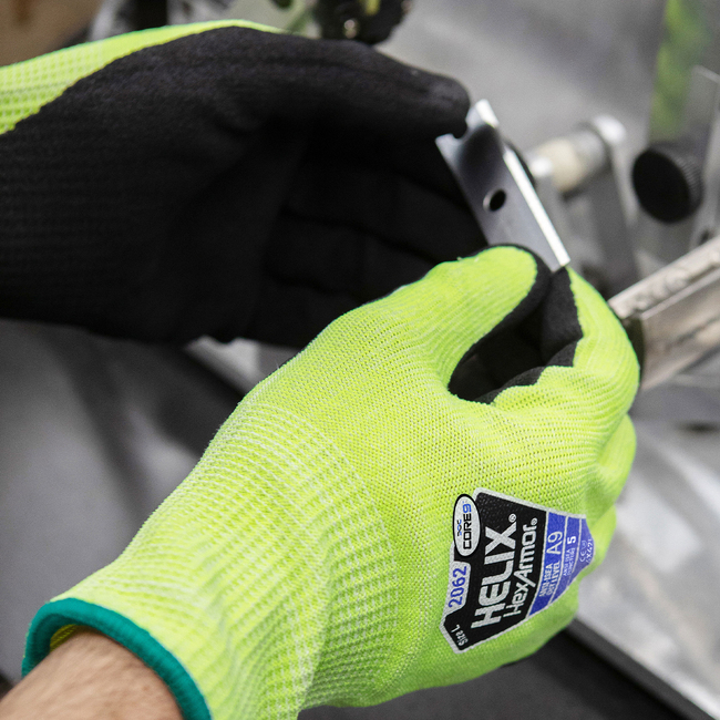 Hands wearing the Helix 2062 hi-vis work gloves are easily handling a sharp metal razor blade.