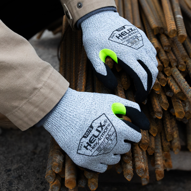 Worker wearing Helix 1075 general-purpose work gloves while working with large metal rods safely. 