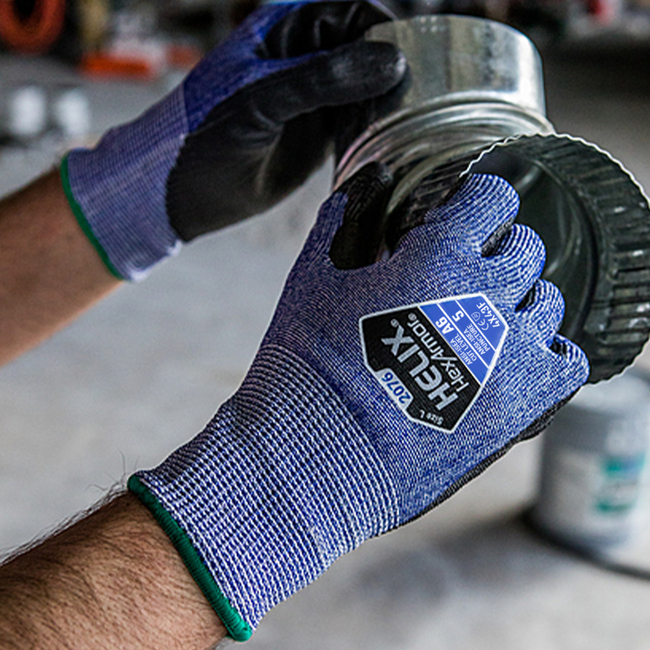Hands wearing the Helix 2076 knit work gloves are easily handling a circular metal pipe with sharp edges.