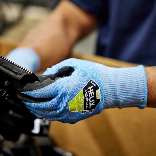Hands wearing the Helix 3022 cut-resistant gloves in an industrial setting using a touchscreen device.