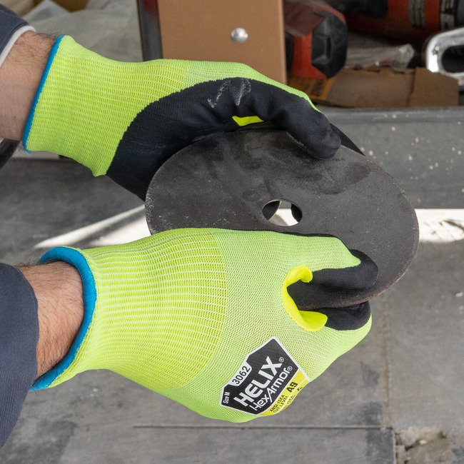 Hands wearing the Helix 3062 cut-resistant gloves handling sharp metal disks.